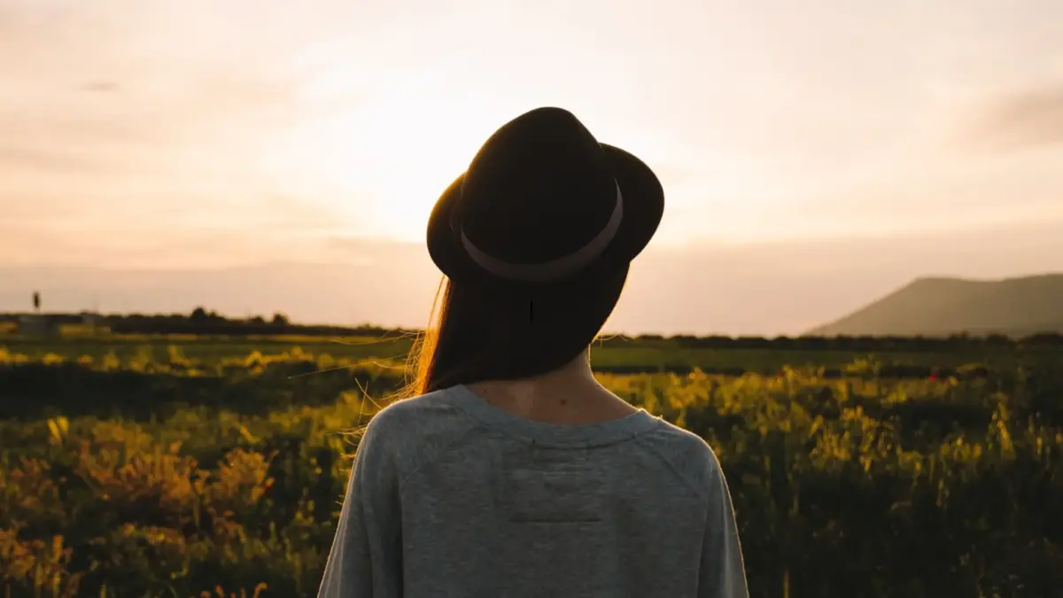 Woman in hat watching sunset over fields.