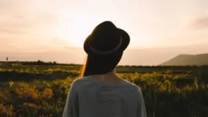 Woman in hat watching sunset over fields.
