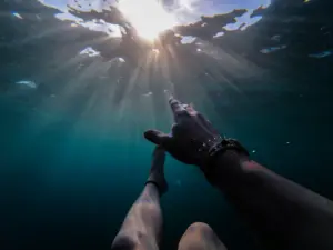 Underwater view, sunrays shining above person reaching up.