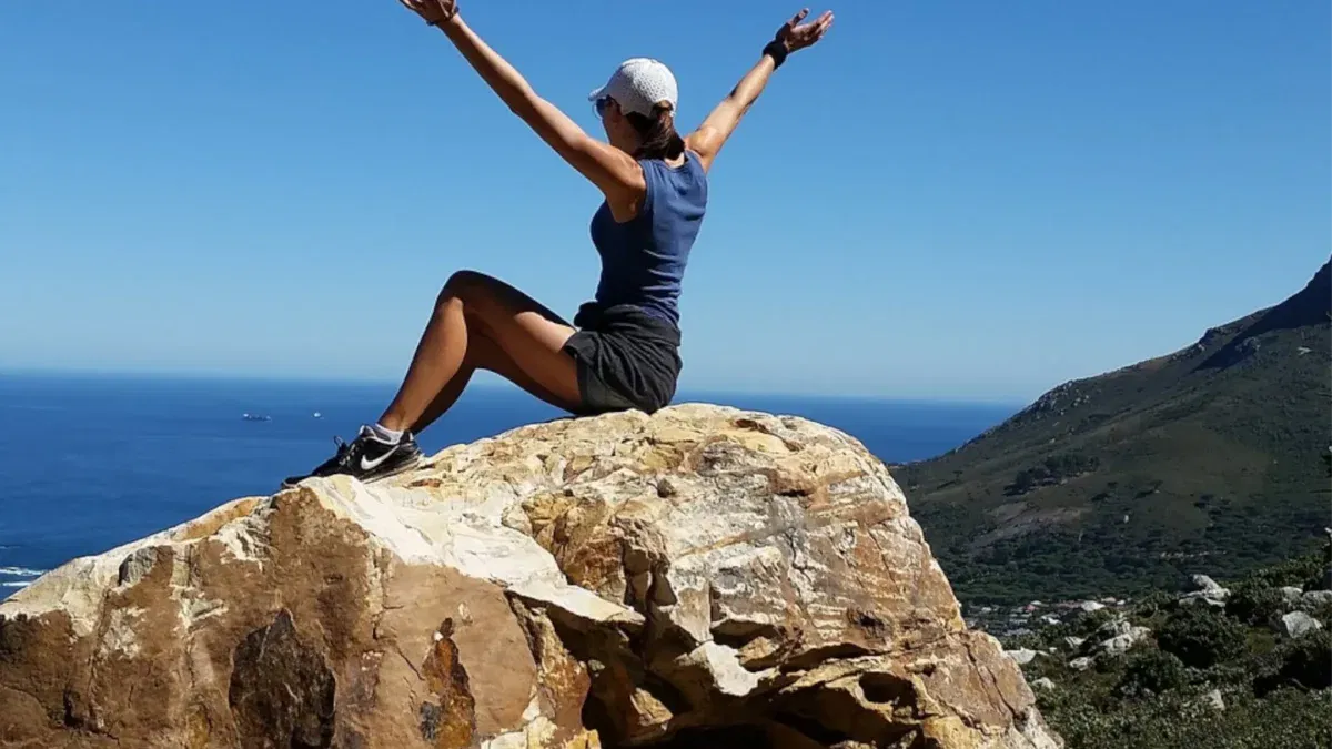 Person on rock celebrating, overlooking the ocean.