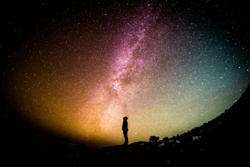 Person stargazing under colorful Milky Way galaxy.