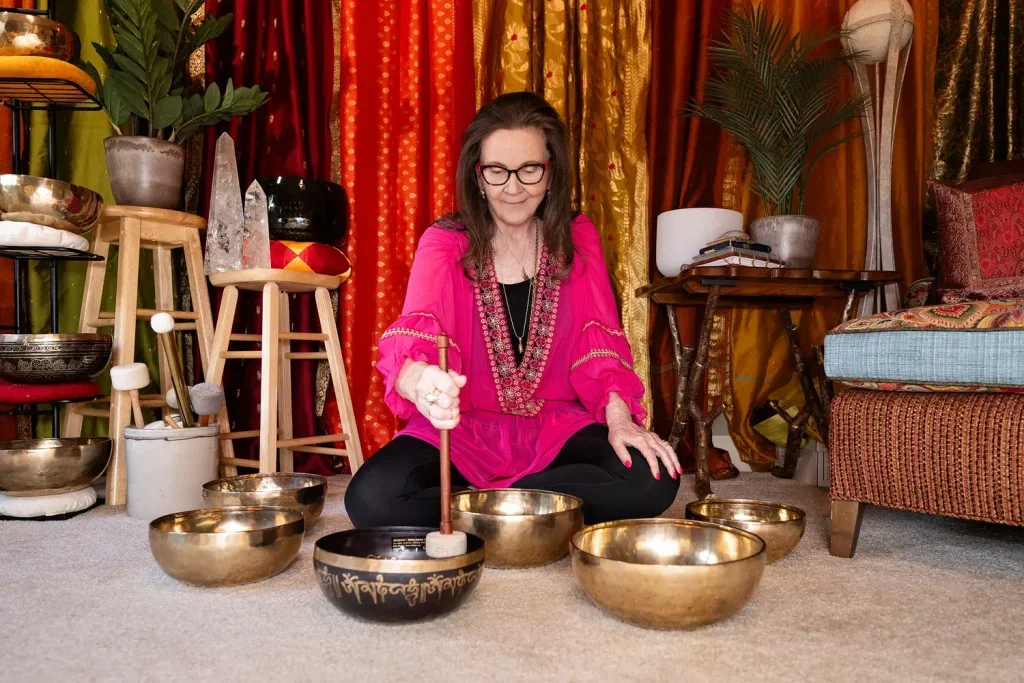 Dorothy Tannahill-Moran seated cross-legged playing Tibetan singing bowls on the studio floor
